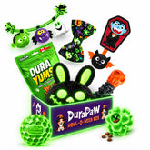 DuraPaw Howl-O-Ween Box Halloween dog toy set featuring a plush black bunny with glowing green eyes, a green squeaky ball, a green ball with a skull face, a green bow tie, a green snake toy, a vampire-shaped treat dispenser, and a green bag of DuraPaw Dura Yums healthy beef treats on a white background.