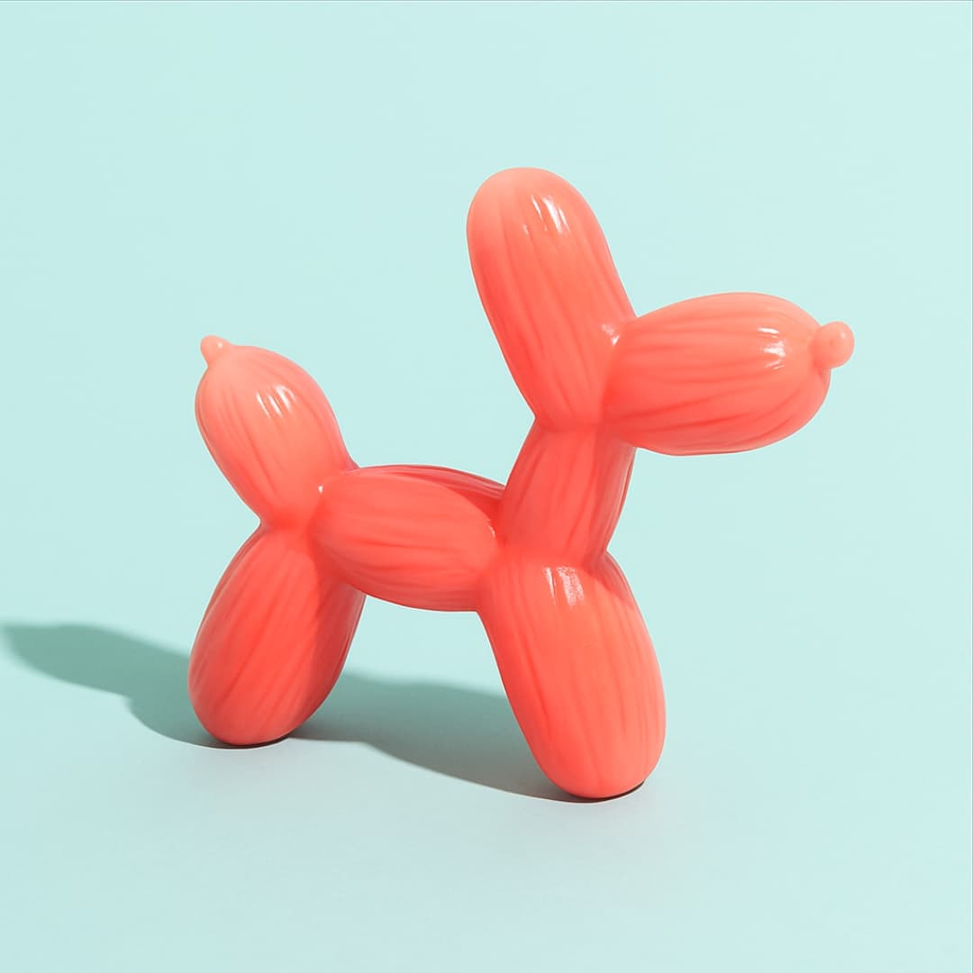 Pink balloon dog-shaped chew toy with glossy finish, shown against a light blue background